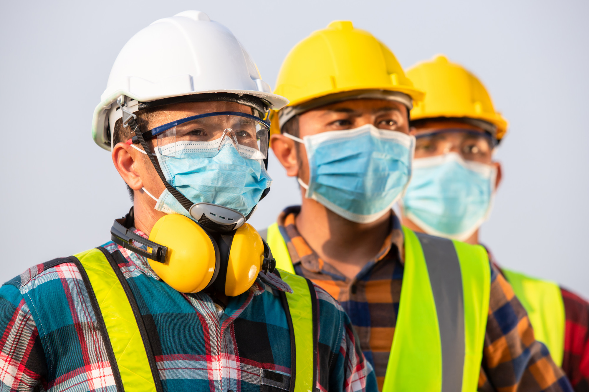 three construction workers wearing masks and safety vests
